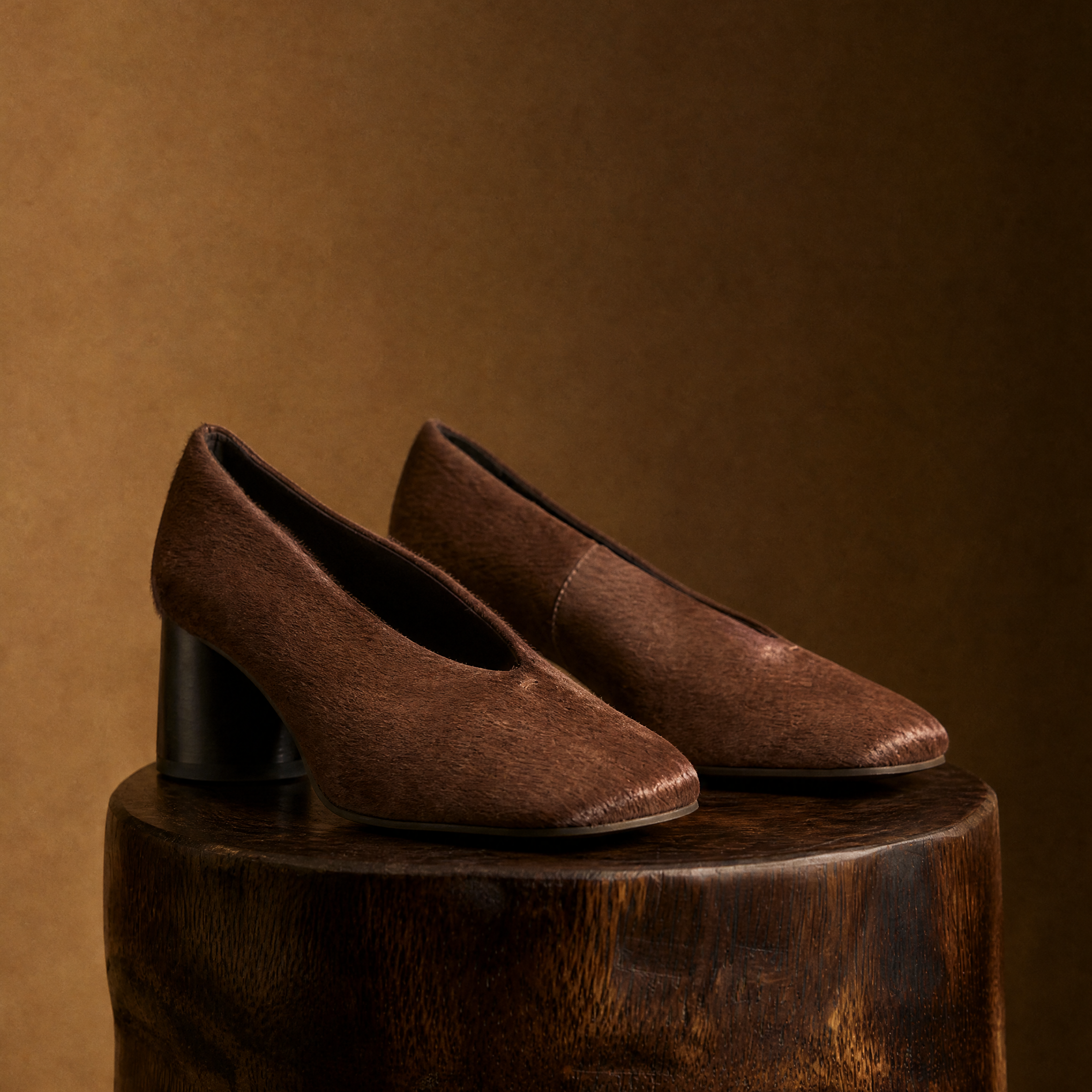 Pair of brown chestnut pony hair heeled shoes on a wooden block against a brown background