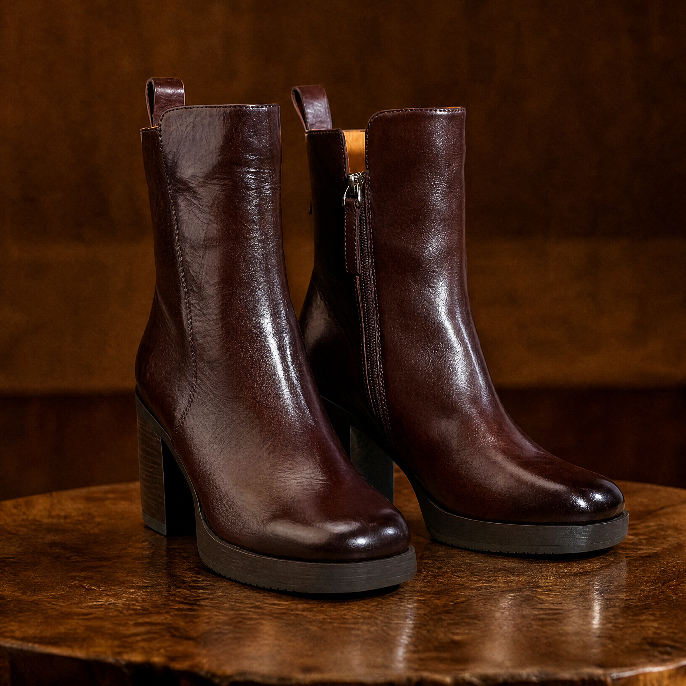 Pair of chestnut leather heeled boots on a wooden surface with a dark brown background
