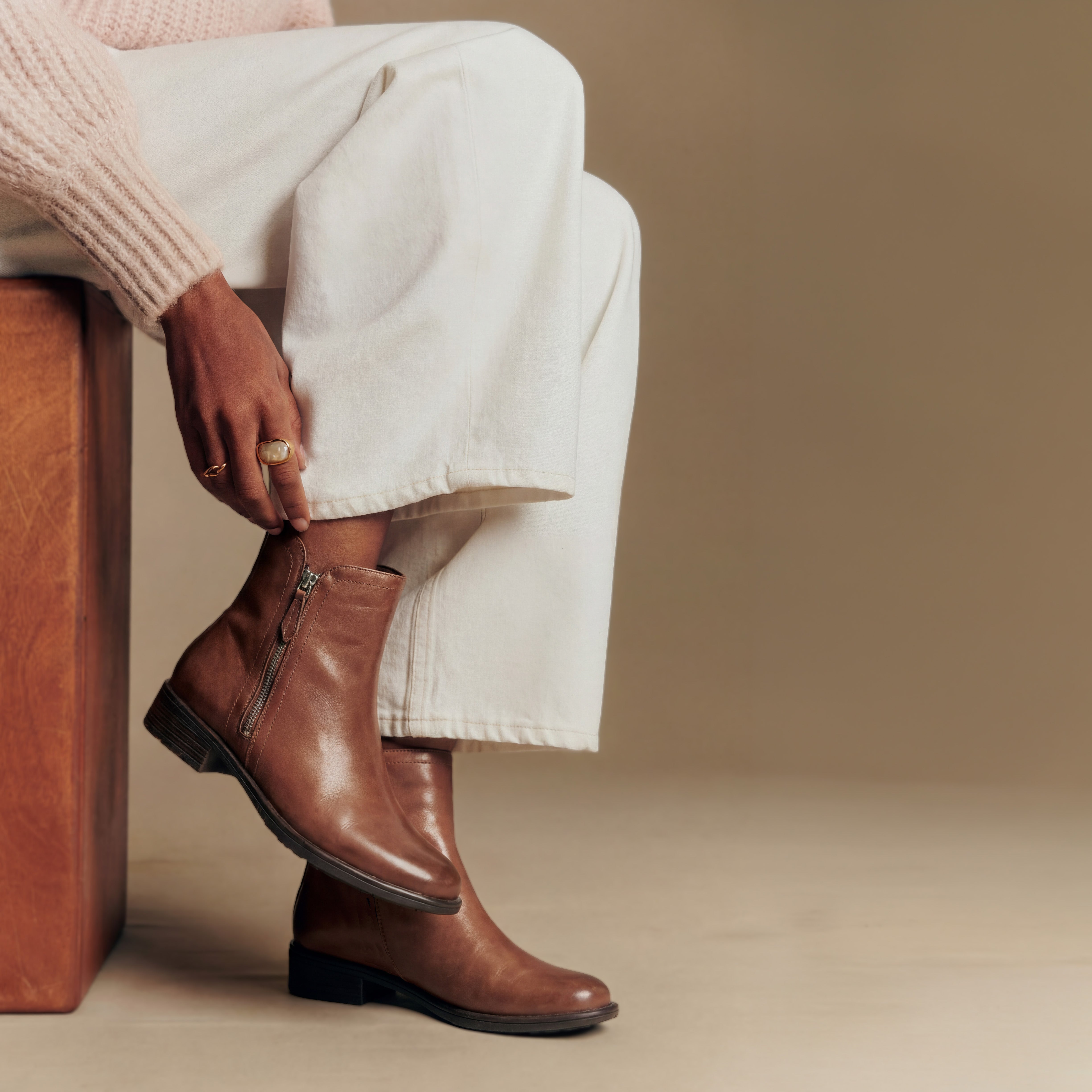 Person wearing dark taupe brown leather ankle boots with outside zip on a neutral background